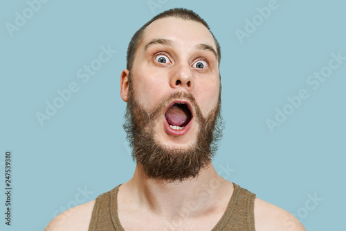 Very surprised scared funny face of a bearded guy with open mouth and big eyes on an isolated background