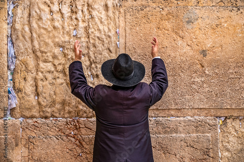 Believing Jew pray near the wall of crying in a big black hat raising his hands uphill