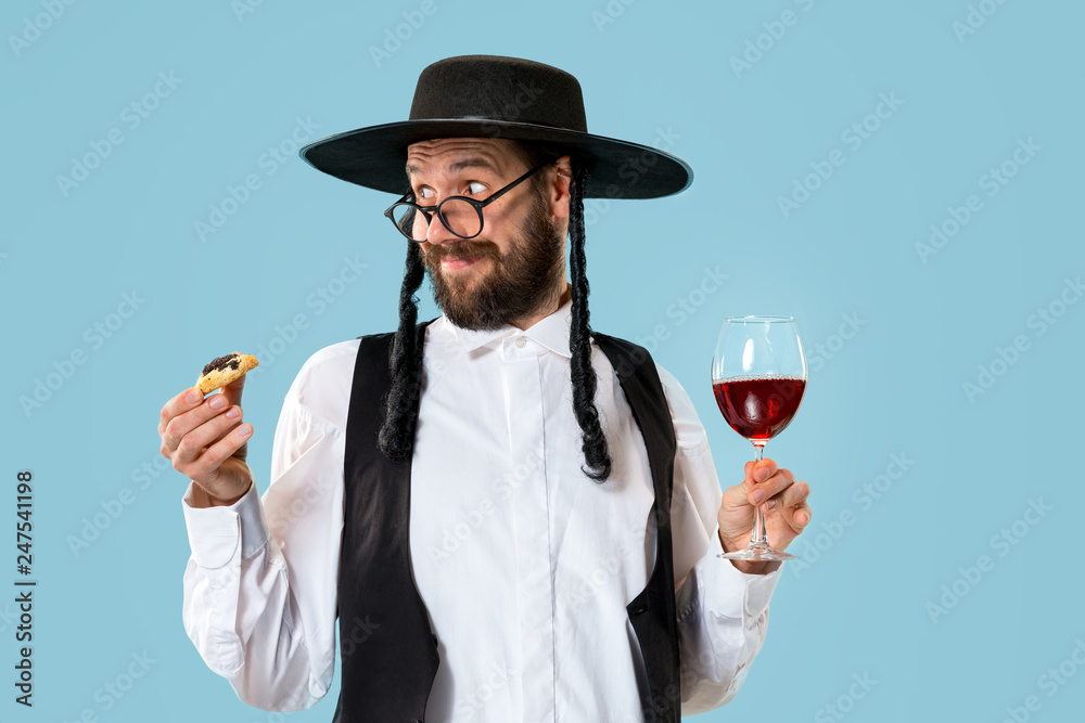 Fototapeta premium The young orthodox Jewish man with black hat with Hamantaschen cookies for Jewish festival of Purim at studio. The purim, jewish, festival, holiday, celebration, judaism, pastry, tradition, cookie