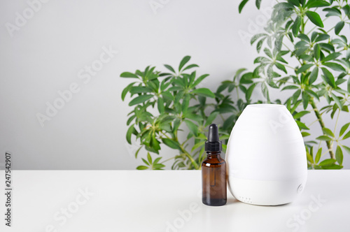 Ultrasonic Oil diffuser with glass amber bottle on white table of schefflera plant background