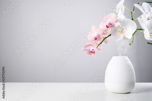 Ultrasonic Oil diffuser and orchid flowers on white table of gray background photo