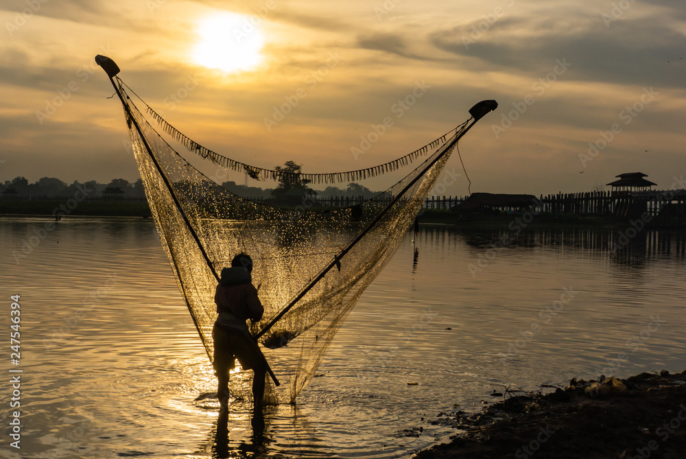 men fishing with triangular scoop net early morning at sunrise near iconic  U-Bein Bridge, on shallow Lake Taungthamanin, Amarapura, Mandalay, Myanmar  Stock Photo