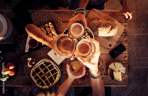 People eat mixed meals at festive table served for party. Friends celebrate with food on wooden table top view. Happy company having lunch, clinking glasses - outdoor friendship concept