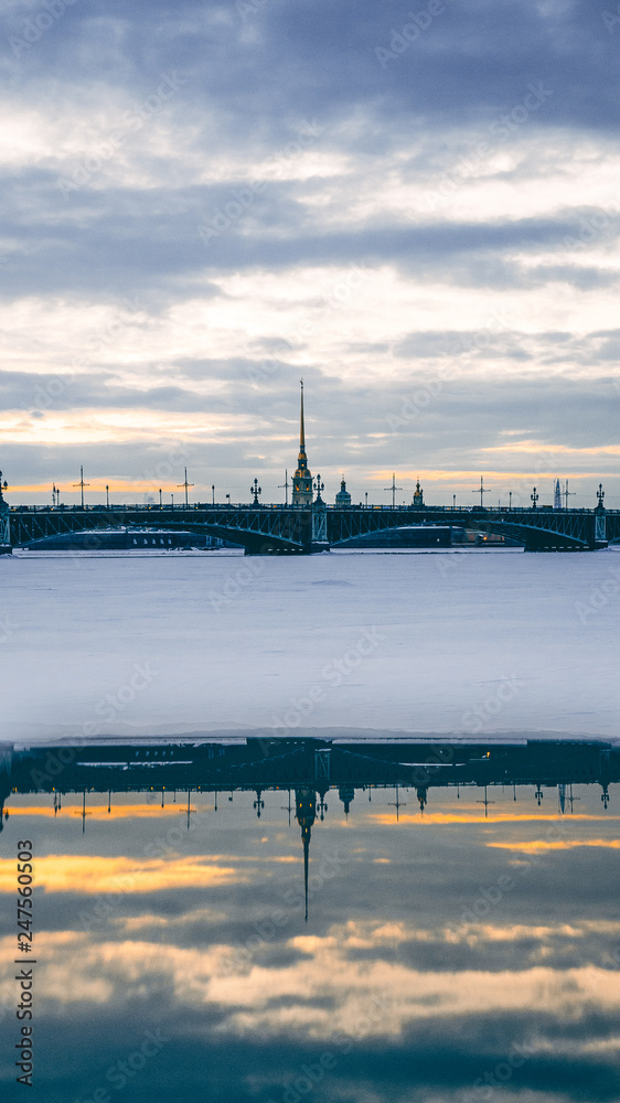 View at Peter-Pavel's Fortress in winter, frozen river in front, cloudy sunset sky, landscape view. Reflection from water