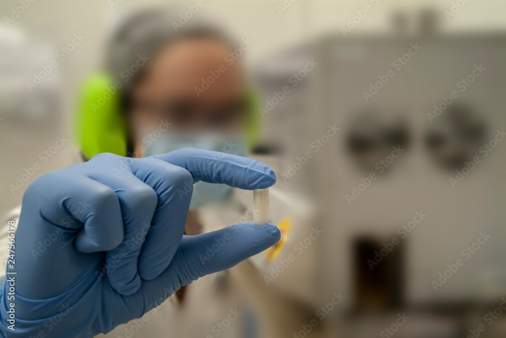 Holding a pill between gloved fingers in the lab Holding a pill between gloved fingers in the lab