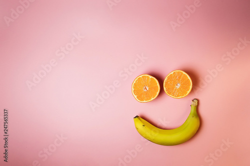 Smiley face with two oranges and a banana with copy space on a pink background