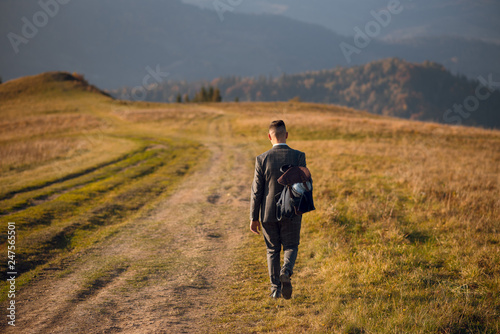 Man in suit and backpack walking down the hill in beautiful autumn mountains on sunny day. © WellStock