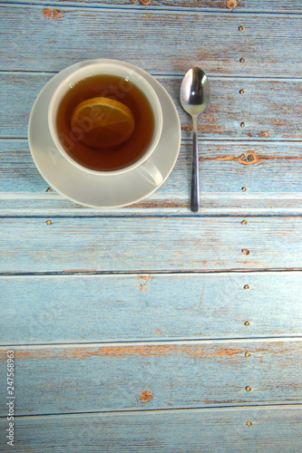 A cup of tea with a slice of lison and a spoon lie on a wooden table. photo