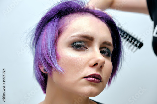 A girl in a gray t-shirt and makeup sitting with wet, purple and short hair on a white background in the middle of the frame. photo
