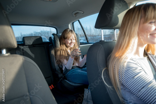 Cute little girl sitting in child car seat playing on tablet and having fun