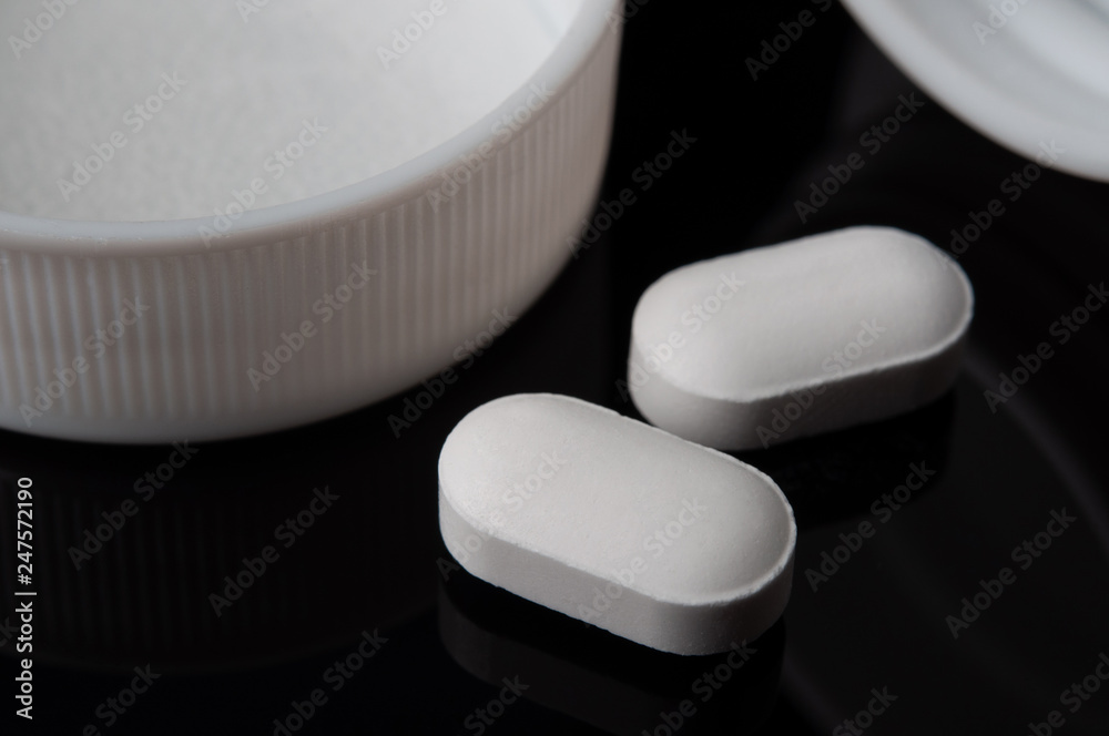 white tablets of medicine pouring out of the pills bottle on black background. closed up and selective focus