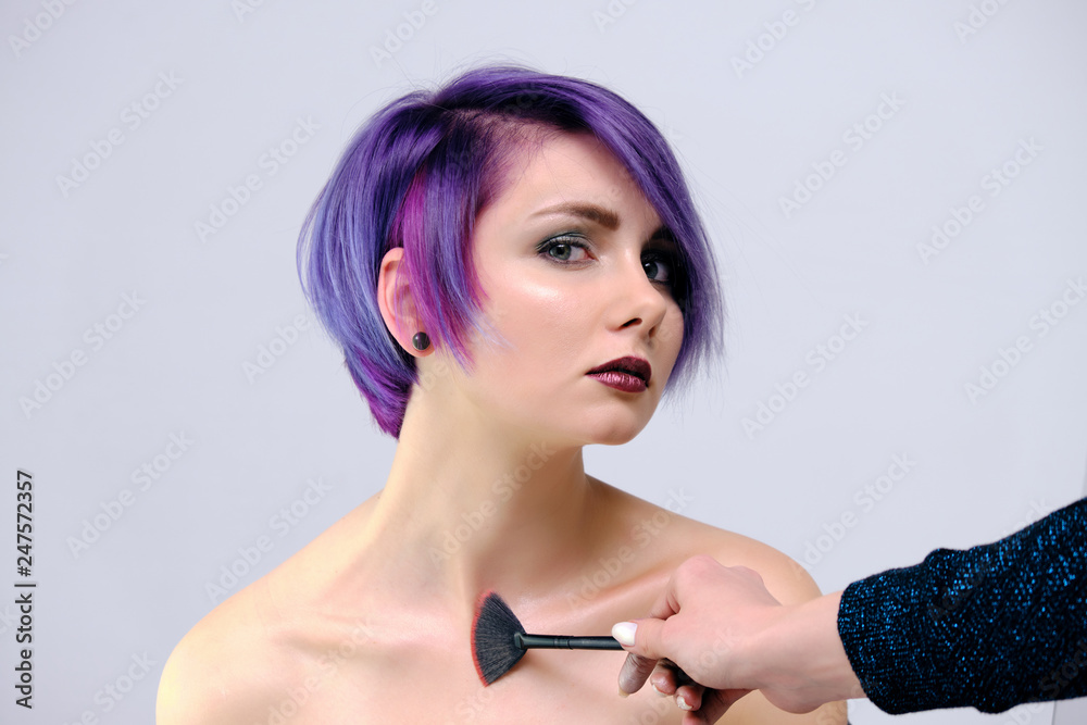 Obraz premium A beautiful, sexy girl with purple hair and a short haircut sits in the middle of the photo with a white background