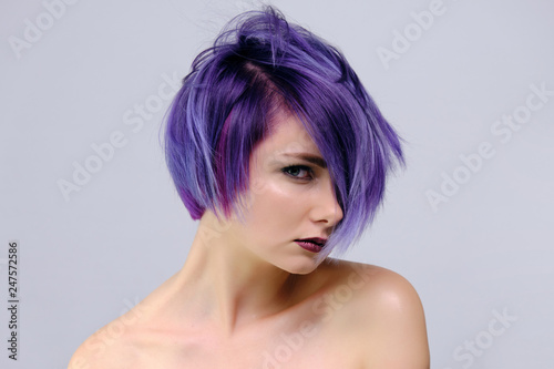 A beautiful, sexy girl with purple hair and a short haircut sits in the middle of the photo with a white background