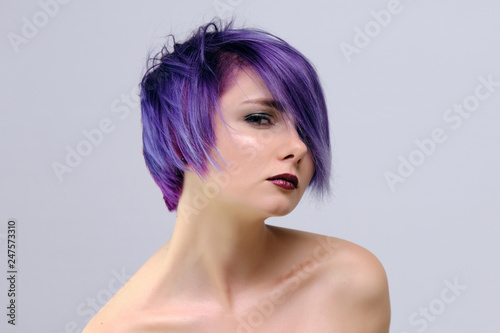 A beautiful, sexy girl with purple hair and a short haircut sits in the middle of the photo with a white background