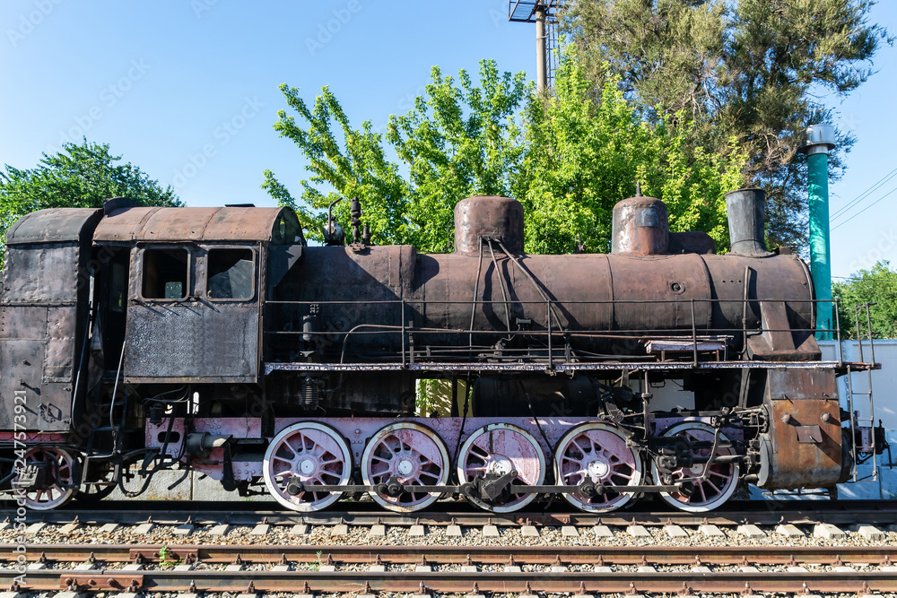 Old rusty steam locomotive beside a railway station platform. Retro train.