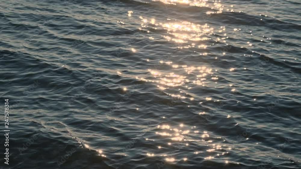 Zeitlupe, slow motion von hellen, sonnigen funkelnden Glitzern auf der Wasseroberfläche und Wellen im goldenen Abendlicht