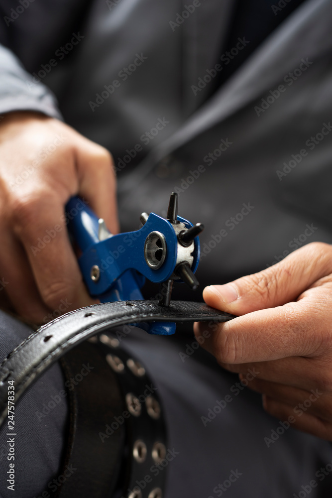 man making a hole in a belt with a leather punch