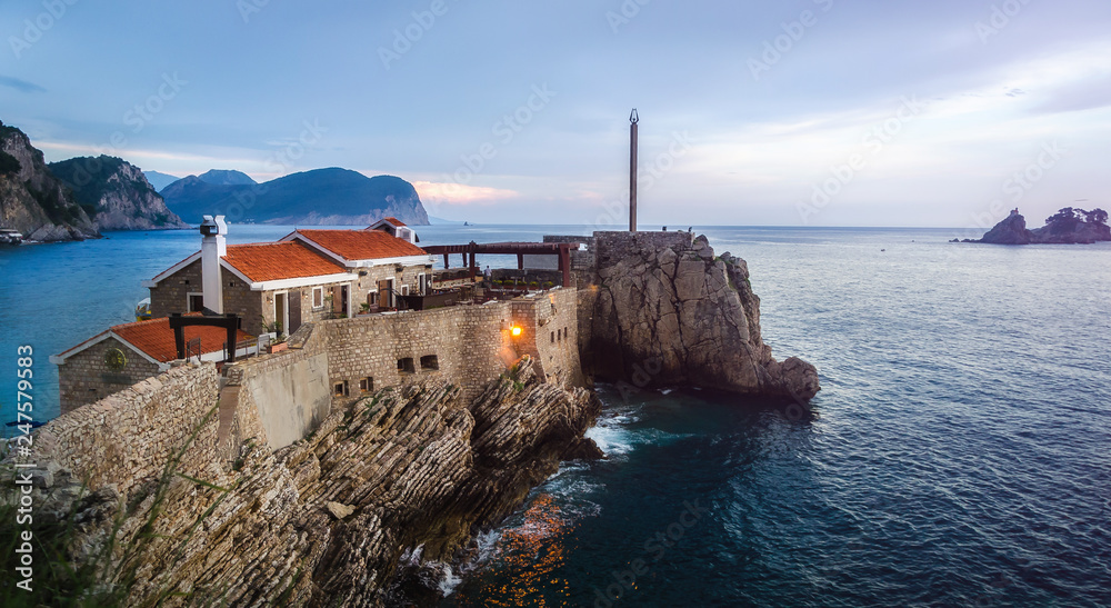 old stone houses with red roofs on a cliff descending into the sea in Petrovac, Montenegro