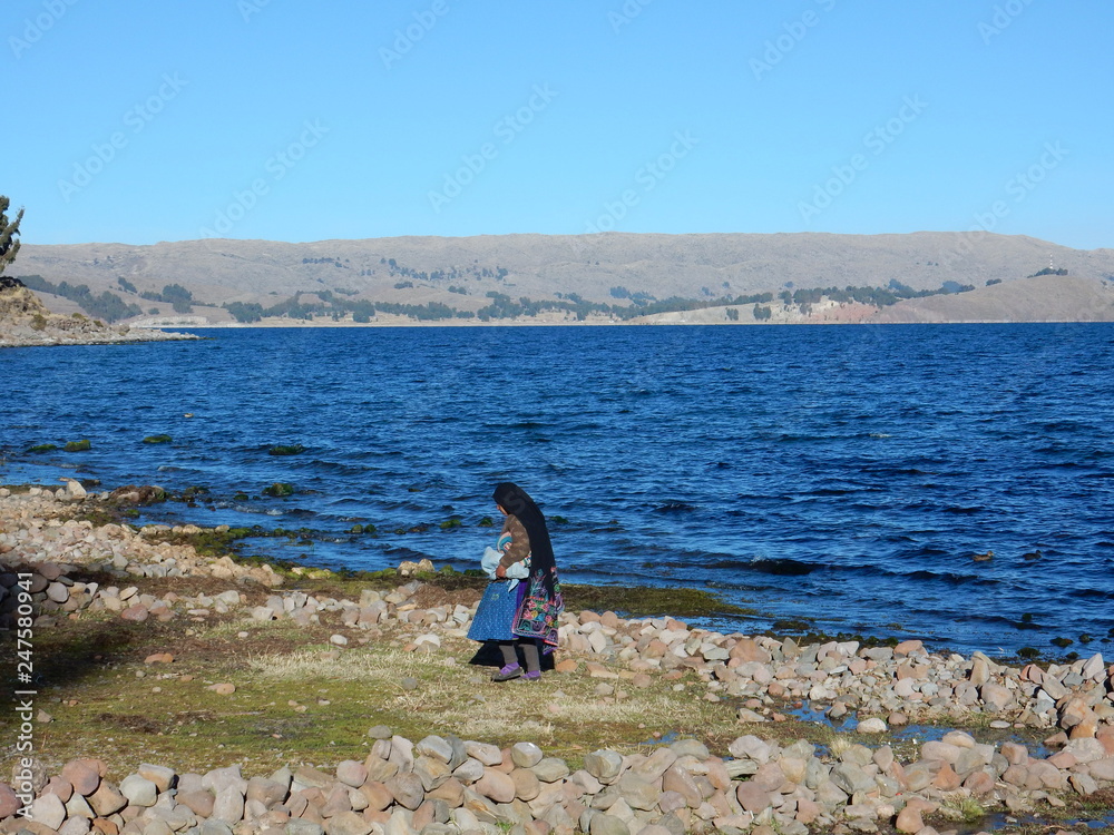 a woman dressed in traditional clothes walking on the beach in Amantani island, Titicaca lake, Peru