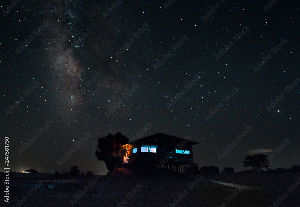milky way over a wooden cabin on an isolates summer beach night