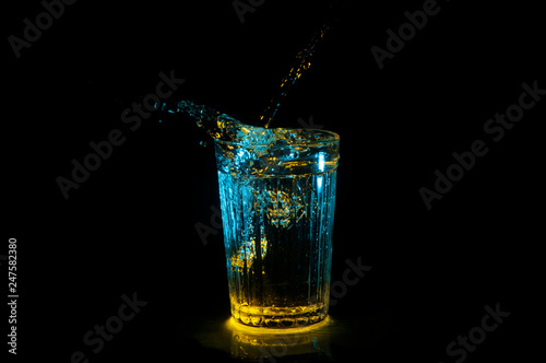 Water splashing from ridged drinking glass in blue and yellow lights isolated on a black background photo