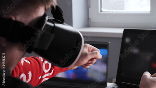 Young guy (male) player in virtual glasses plays (relaxes) against him 2 game monitors, he moves his hands seeing the movement with glasses. Concept of: Lifestyle, Underworld, 3d, Virtual reality