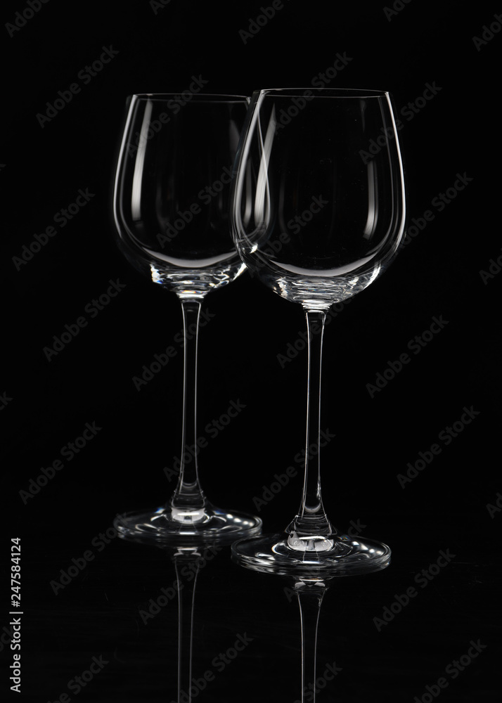 Two wine glasses on a black background with beautiful highlights, one in front of the other; close-up