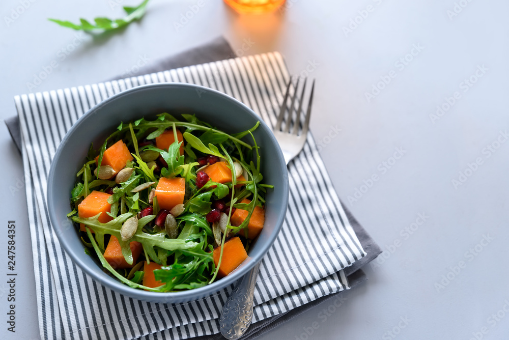 Salad with arugula,pumpkin and pomegranate seeds on gray wooden background. Vegetarian food concept. Selective focus. Salad with arugula,pumpkin and pomegranate seeds on gray wooden background. Vegetarian food concept. Selective focus.