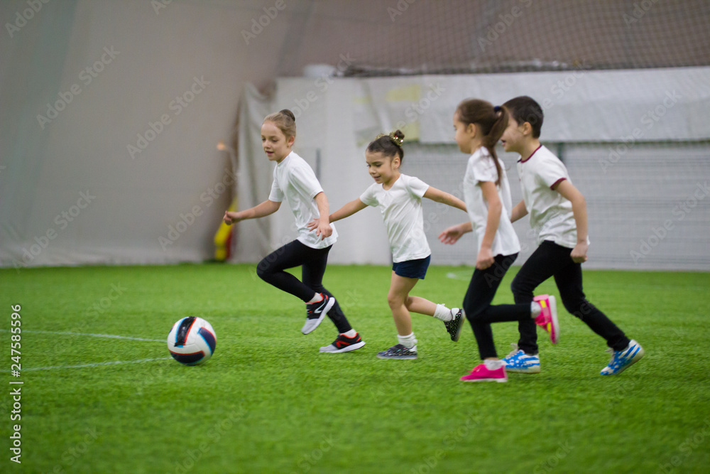 Children playing football indoors. Kids running on the field after the ball