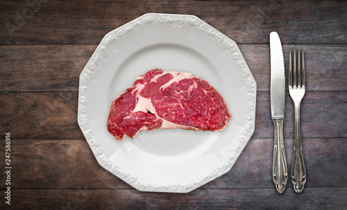 red meat / raw steak on plate on wooden background with knife and fork -