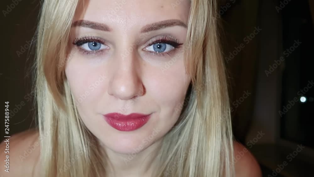 young beautiful blonde woman with bright blue big eyes and red lips flirts at the camera, raises one eyebrow and seduces with her eyes, close-up portrait on a dark background, slow motion young beautiful blonde woman with bright blue big eyes and red lips flirts at the camera, raises one eyebrow and seduces with her eyes, close-up portrait on a dark background, slow motion