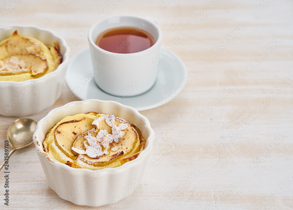 Apple cake and cup of tea on white wooden table in kitchen. Delicate curd dessert with apples, almond flakes and cinnamon, side view Apple cake and cup of tea on white wooden table in kitchen. Delicate curd dessert with apples, almond flakes and cinnamon, side view