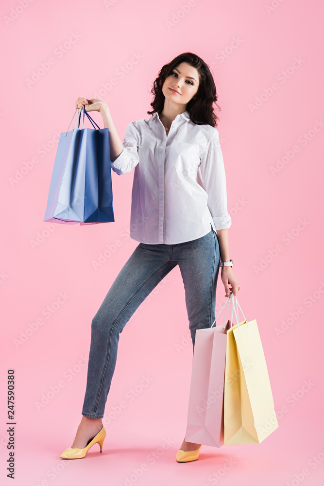 smiling brunette girl holding shopping bags, isolated on pink