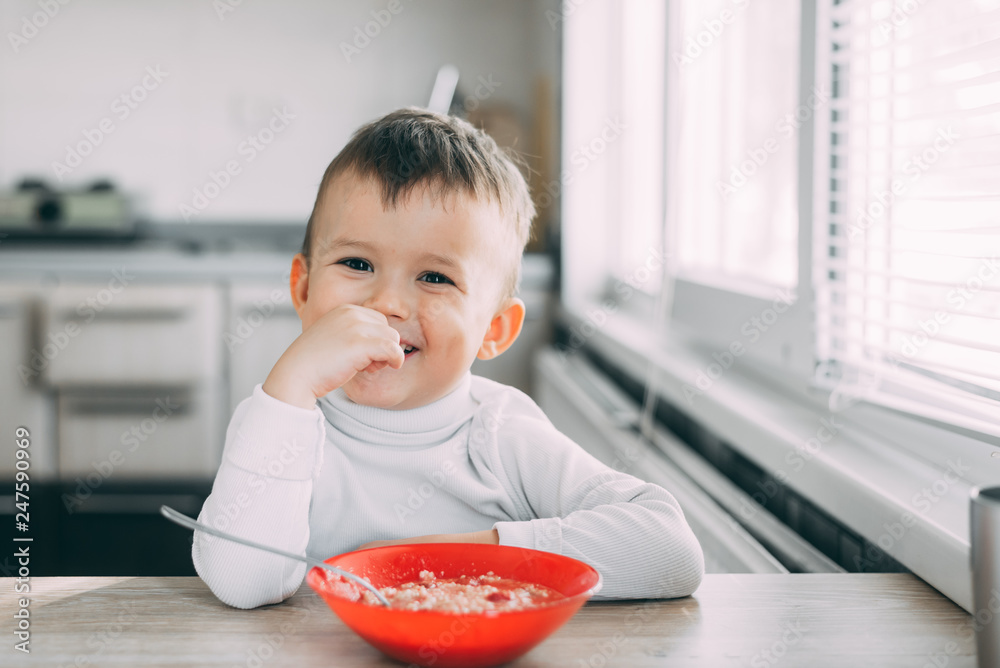 A child in the kitchen eating their own oatmeal with a red plate