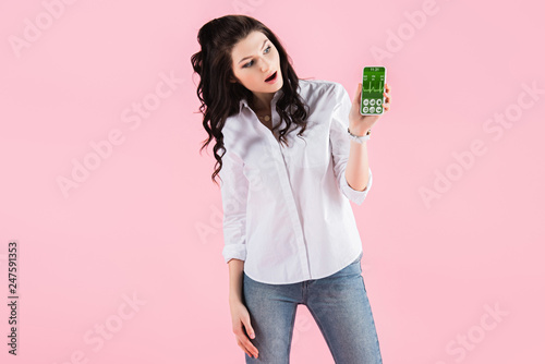 shocked woman showing smartphone with health data on screen, isolated on pink