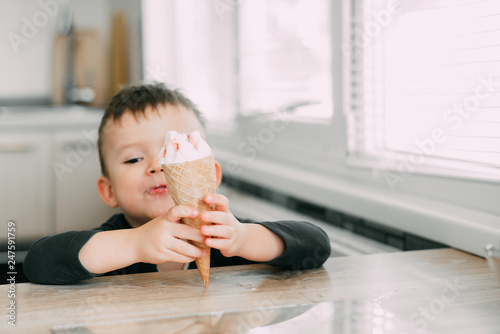 A child in a dark-blue t-shirt in the bright kitchen eating a waffle ice cream cone in the summer house photo