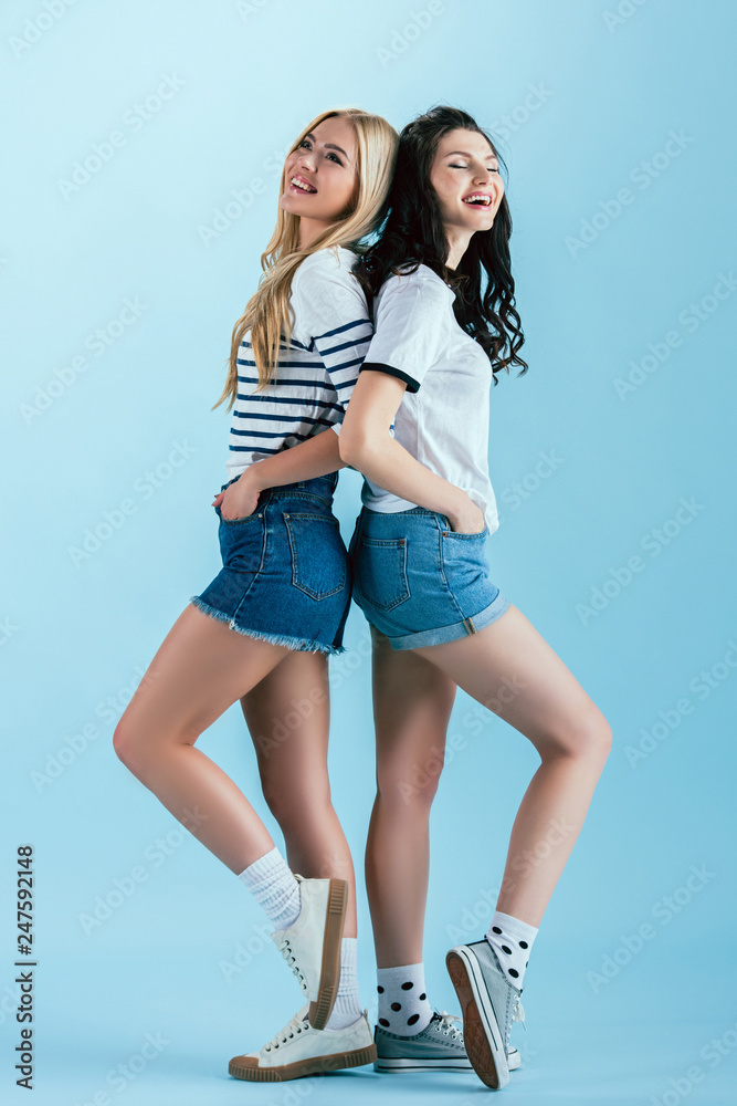 Laughing girls posing with hands in pockets on blue background Laughing girls posing with hands in pockets on blue background