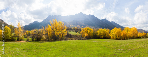 Vista panoramica de Paisaje  otoñal de prados verdes arboledas y montañas rocosas  al fondo. Con pequeño pueblo escondido entre los arboles