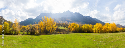 Vista panoramica de Paisaje  otoñal de prados verdes arboledas y montañas rocosas  al fondo. Con pequeño pueblo escondido entre los arboles photo