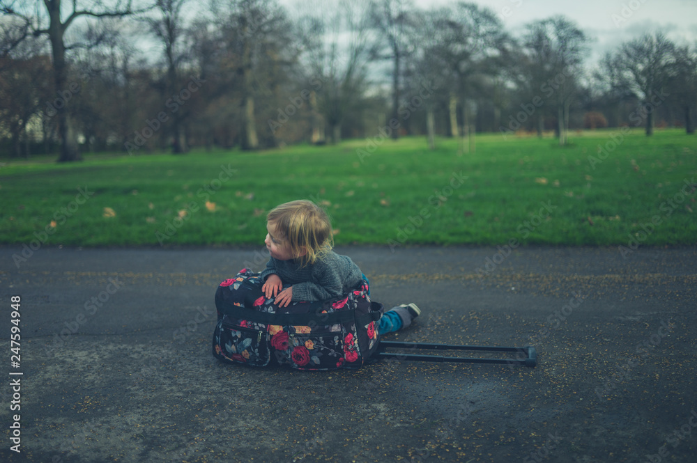 Little toddler resting on suitcase in park Little toddler resting on suitcase in park
