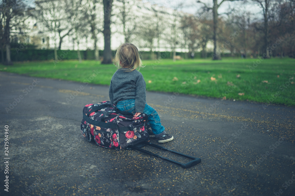 Little toddler resting on suitcase in park Little toddler resting on suitcase in park