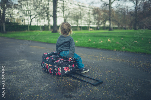 Little toddler resting on suitcase in park © LoloStock