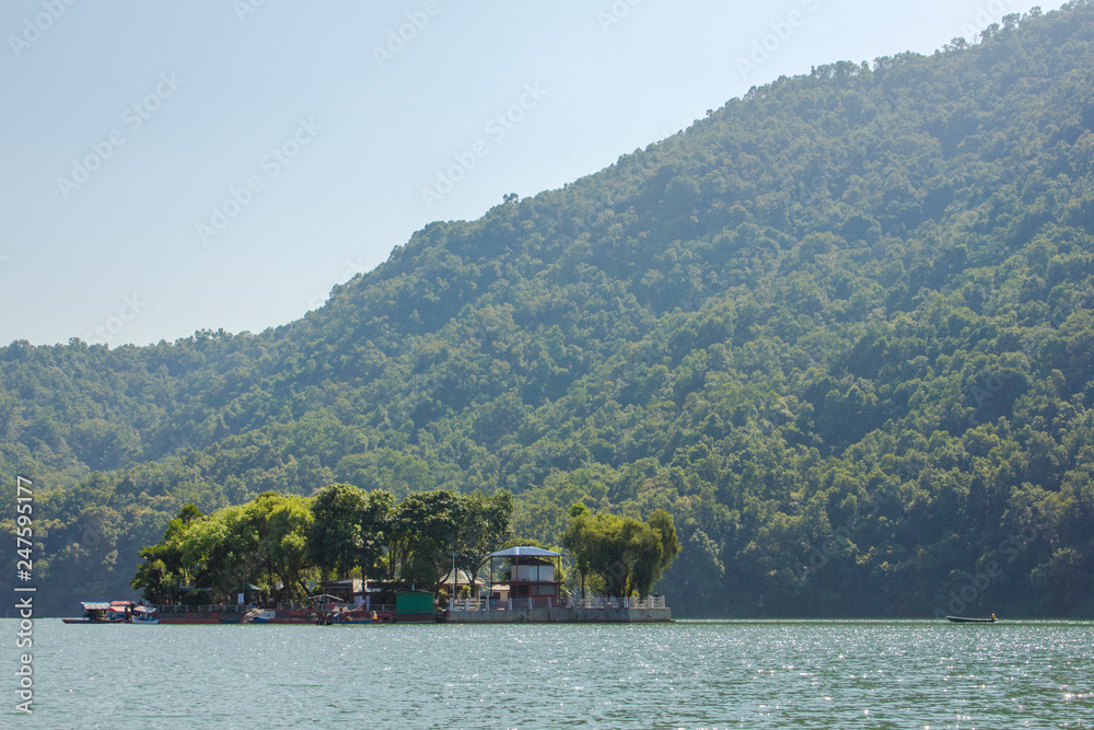 island on the lake with houses and trees on the background of green mountains and blue sky