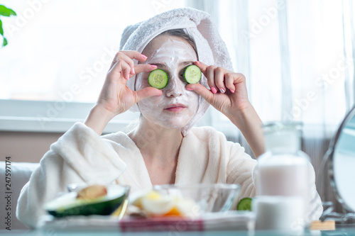 Beautiful young woman with natural cosmetic mask and cucumber slices on her face. Skin care and Spa treatments at home