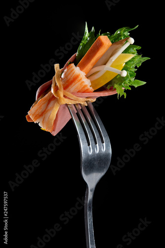 Organic vegetables roll with green salad on steel fork isolated on black background