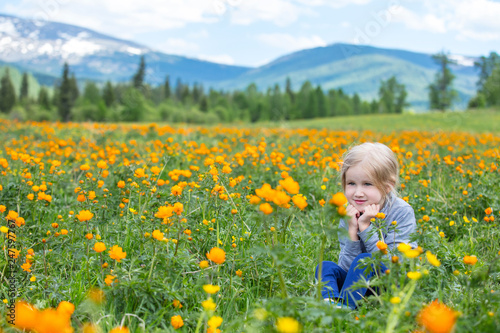 Little cute baby girl is beautiful and happy, smiling in summer in the meadow against the mountains with snow