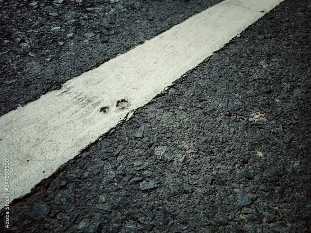 Fototapeta premium A cracked on asphalt road. The white painting is closed up.