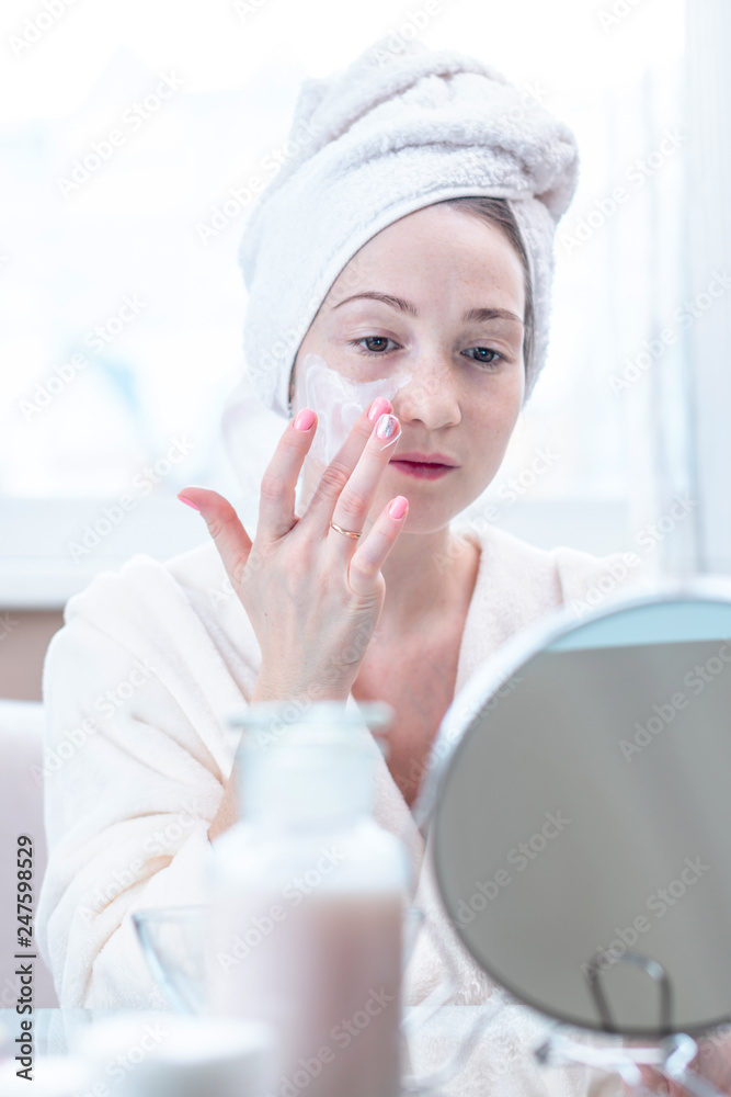 Beautiful happy young woman applying cream on face moisturizing the skin. Hygiene and care for the skin at home Beautiful happy young woman applying cream on face moisturizing the skin. Hygiene and care for the skin at home