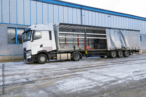 Truck and semi-trailer with an exposed tarpaulin during unloading. Transport and unloading.