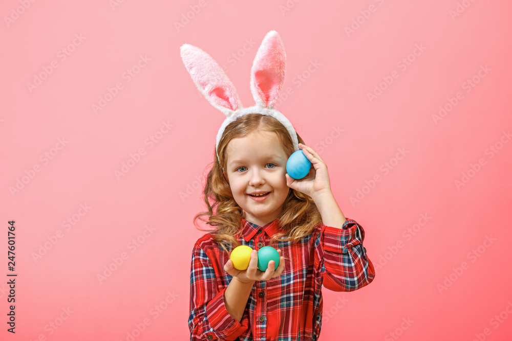 Cheerful little kid girl with bunny ears with easter eggs on a colored background.